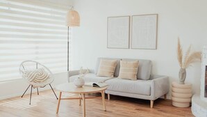 En moderne stue med sofa, rundt sofabord, stol og gulvlampe. To billeder hænger på væggen, og der står en vase med pampasgræs på et sofabord.