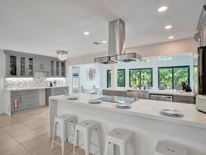 A modern kitchen with a large island, grey cabinets, and a view of greenery outside. - Rent Luxe 5 Star 5 Bed + Heated Pool + All New Pool Lounge Area Stunning!  (Fort Lauderdale)