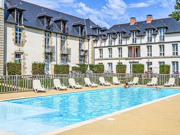 A hotel with a swimming pool, multiple balconies, and lounge chairs.