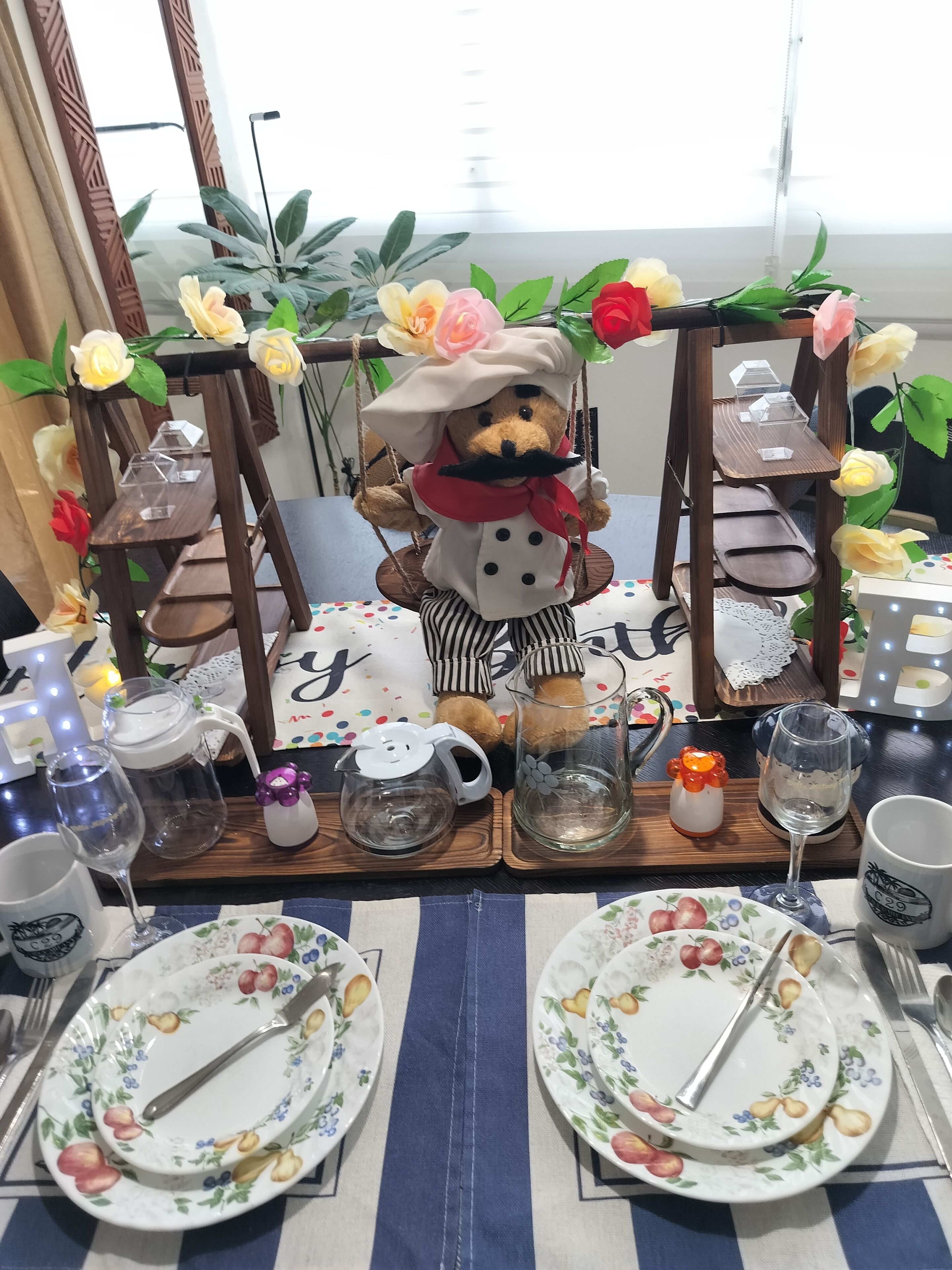 A dining table set with plates, cutlery, and a teddy bear in a chef's outfit.