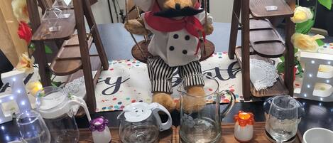 A dining table set with plates, cutlery, and a teddy bear in a chef's outfit.