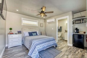 Un dormitorio con cama, mesita de noche, cómoda, ventilador de techo y zona de kitchenette.