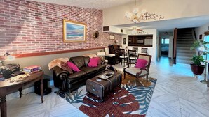 A living room with a brick wall, a sofa, a coffee table, and a rug. There is a staircase leading to an upper level.
