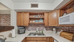 A kitchen with wooden cabinets, a microwave, a toaster, and a brick backsplash.
