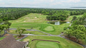 Ein Golfplatz mit Teich, umgeben von dichter Baumvegetation und einem Gewässer im Hintergrund.