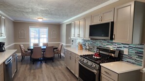 A modern kitchen with a dining area, featuring a large stove, microwave, and a TV.