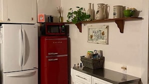 A kitchen with a white refrigerator, a red microwave, white cabinets, and a shelf with various items.