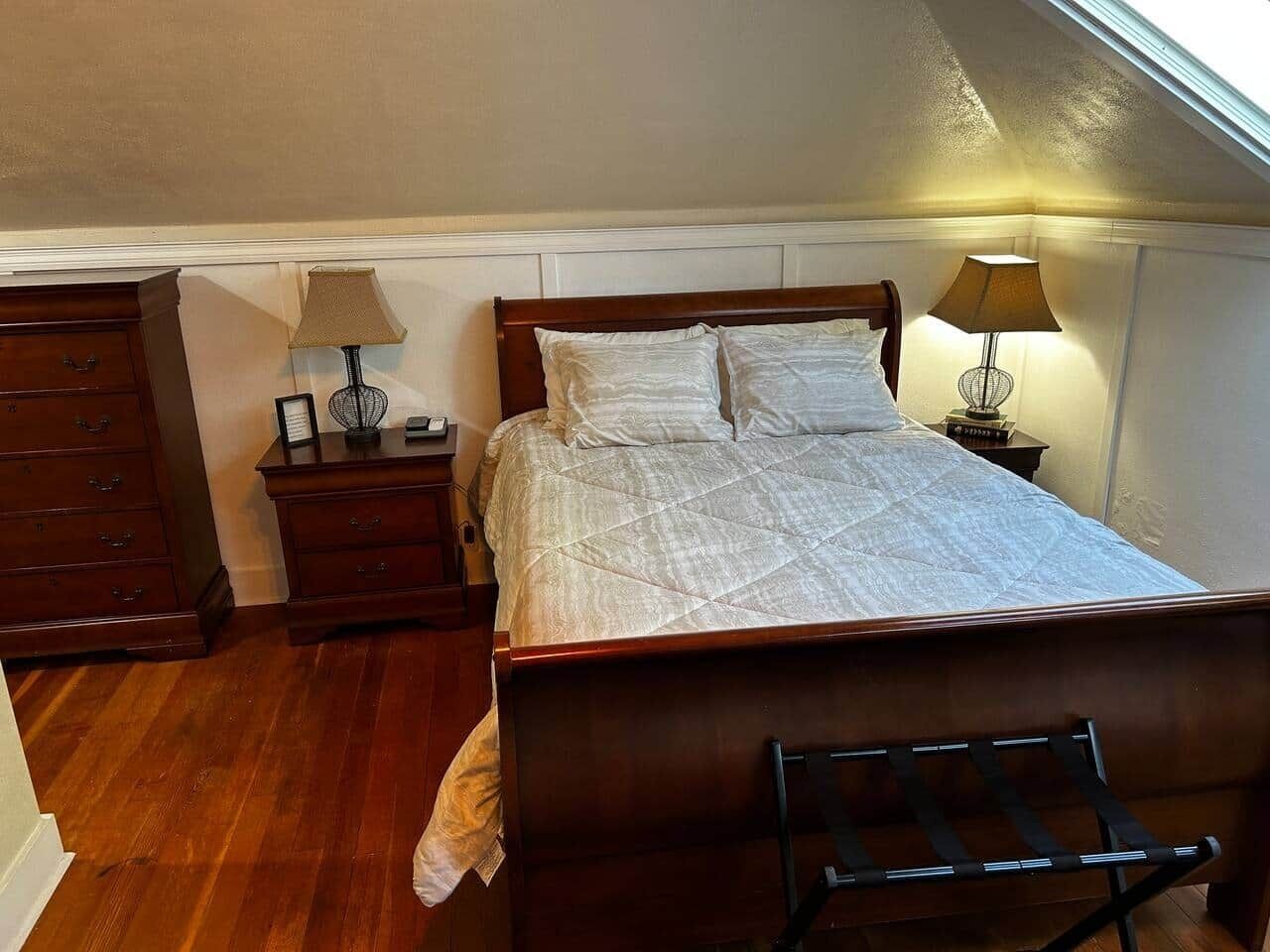 Ein Schlafzimmer mit einem hölzernen Bett, zwei Nachttischen, einem Beistelltisch und einem Sessel.