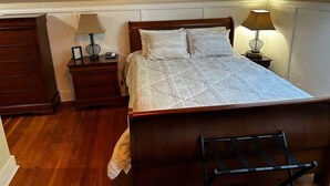 A bedroom with a wooden bed, two bedside tables, a nightstand, and a chair.