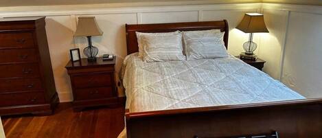 Ein Schlafzimmer mit einem hölzernen Bett, zwei Nachttischen, einem Beistelltisch und einem Sessel.