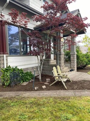 A residential building with a porch, a tree with red leaves, and a wooden chair.