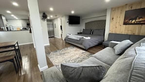 Una sala de estar moderna con un sofá gris, una cama con ropa de cama gris y una pared de madera con un televisor montado.