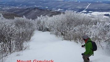 Un escursionista su un sentiero innevato con vista su montagne lontane e una strada.