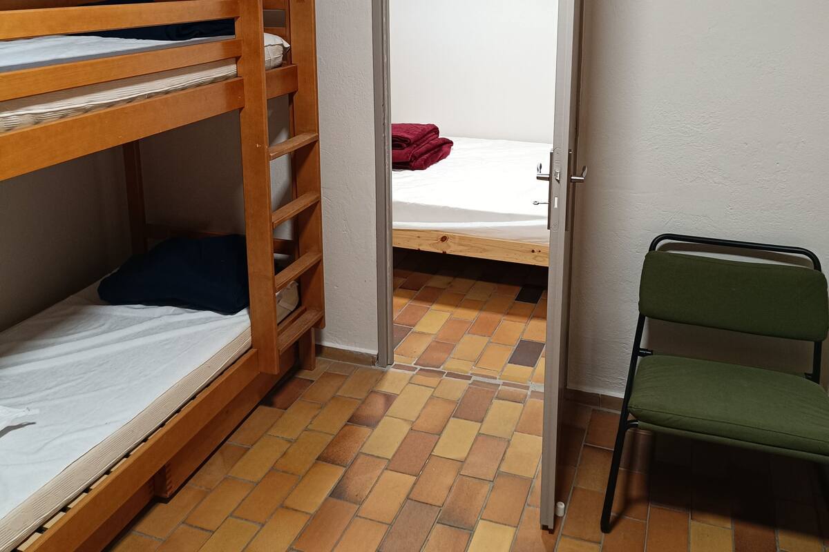 Ein Schlafsaalzimmer mit zwei Etagenbetten, einem Stuhl und einer Tür zu einem weiteren Raum.
