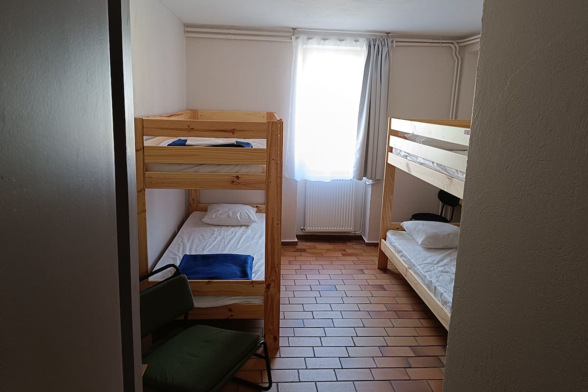 Ein kleiner, kompakter Raum mit zwei Etagenbetten, einem Heizkörper, einem Fenster mit Vorhängen und einem Fliesenboden.