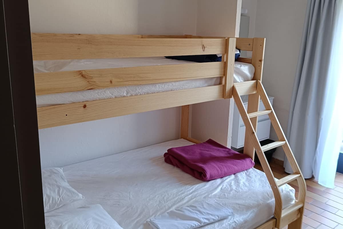 Ein Etagenbett mit Holzleiter, einer weißen Matratze und einer lila Decke.