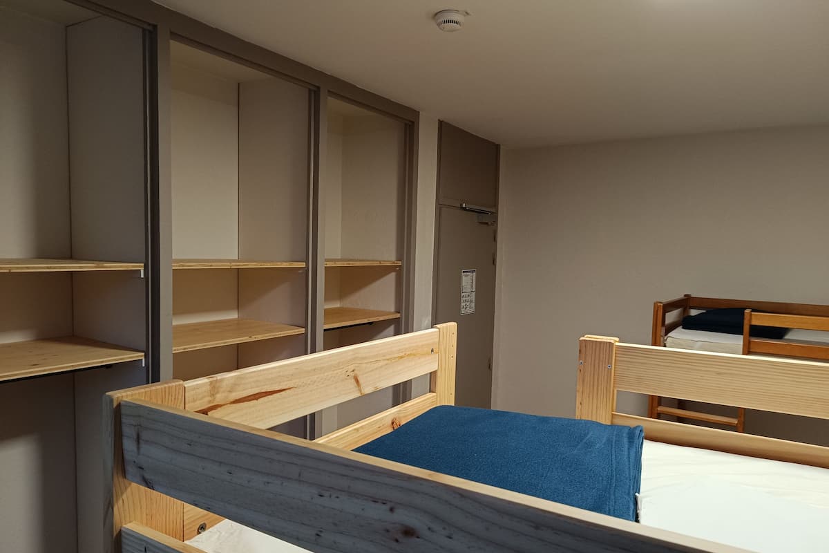 Ein Zimmer mit zwei Holzbettklappen, einem Schrank mit vielen Ablagen und einer Tür mit einem Schild.
