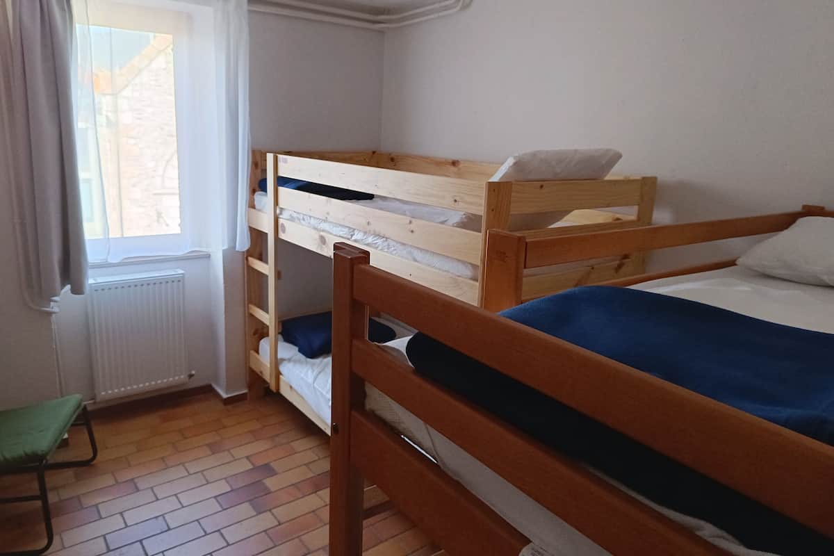 Ein Zimmer mit zwei Etagenbetten, einem mit Vorhängen versehenen Fenster, einem Heizkörper und einem grünen Stuhl.