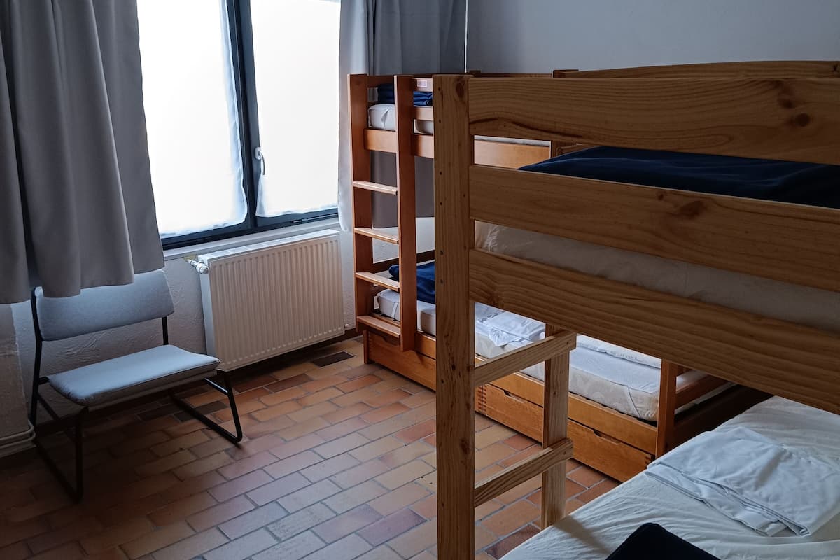 Ein Zimmer mit Etagenbetten, einem Sessel, einem Heizkörper und einem Fenster mit Vorhängen.