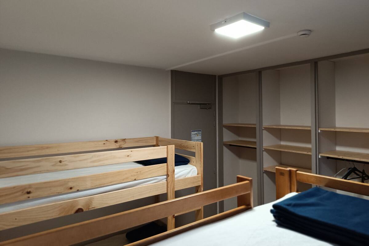 Ein Zimmer mit zwei Holzbettställen, einem kleinen Regal und einem Schrank mit geöffneten Türen.