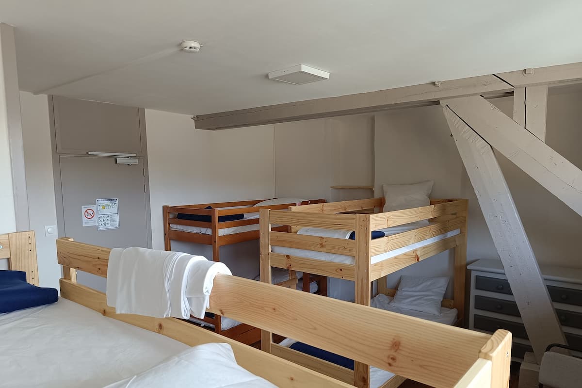 Ein Schlafsaalzimmer mit Etagenbetten, einer weißen Decke, einem sichtbaren Rauchmelder und einer Tür mit einem Hinweisschild.