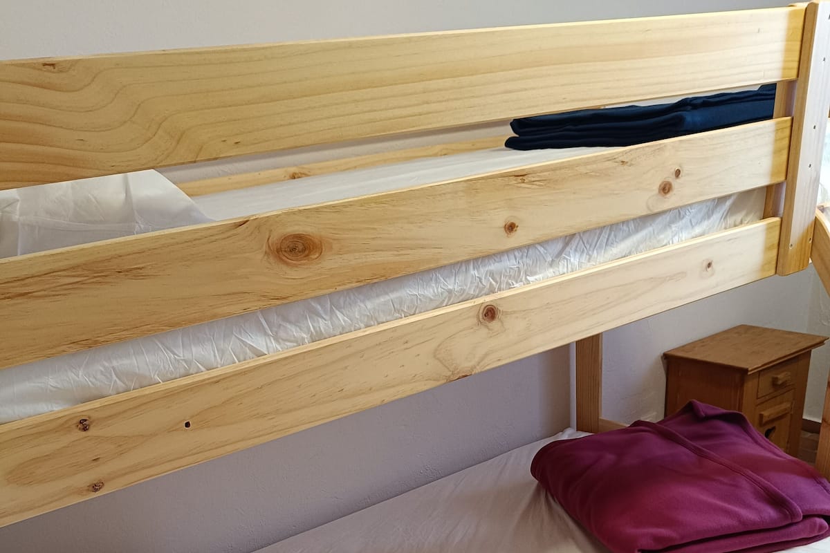 Ein hölzernes Etagenbett mit Matratze und Kissen, ein kleiner Nachttisch aus Holz und eine violette Decke.