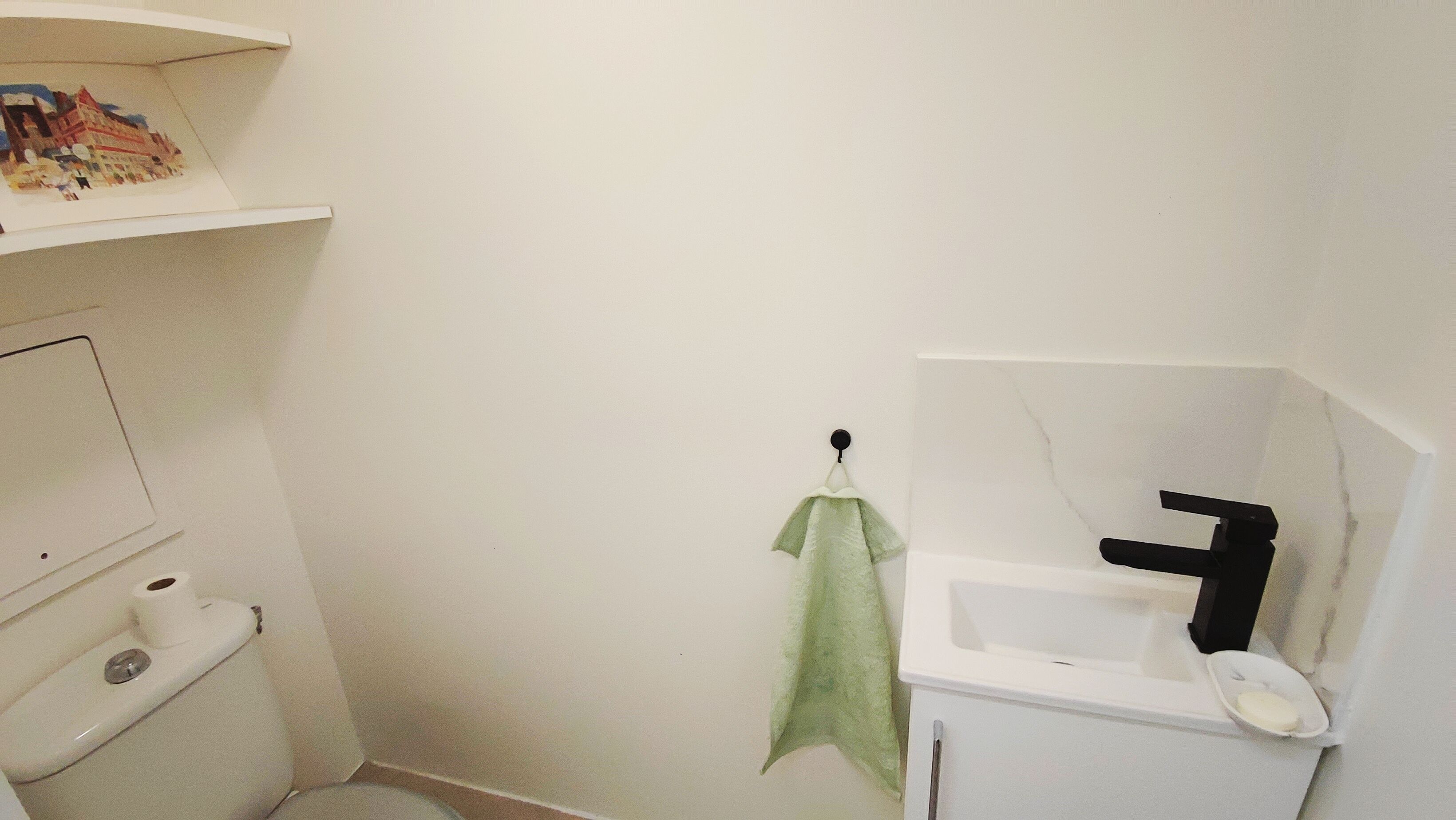 Un baño pequeño con inodoro, lavamanos y un estante sobre el inodoro.