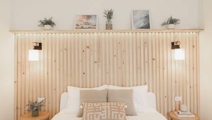 A bedroom with a wooden slat headboard, a large bed with white bedding, two bedside tables with lamps, and three framed pictures on the wall. - Blvd Sunset. . . Beachfront Condos (Ensenada)