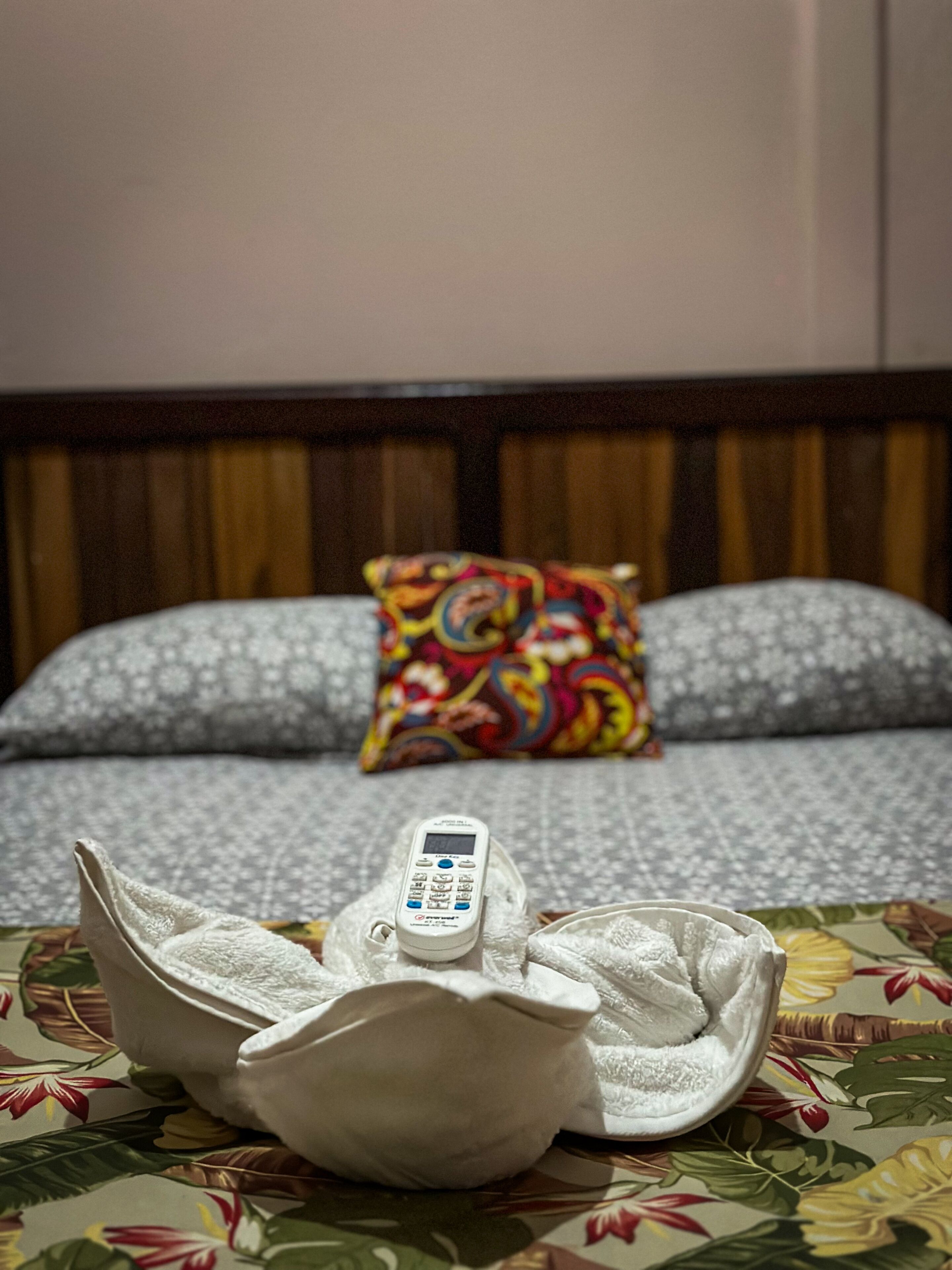 A bed with a patterned bedspread, a pillow with a colorful design, and a white electronic device on the bed.
