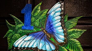 A stained glass window with a blue butterfly and leaves, and the number 1. - Cabinas Tropicales (Puerto Jiménez)