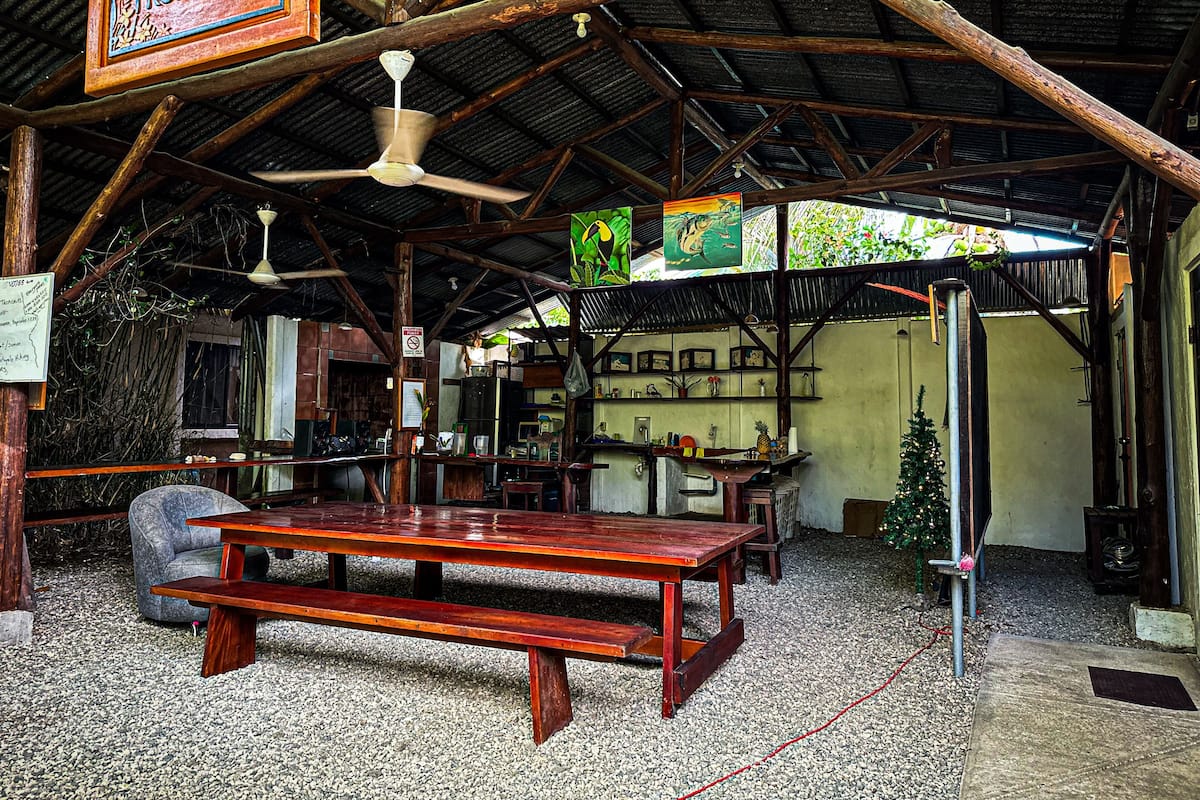 Ein rustikales Holzinterieur mit Holztisch und -bänken, einem Deckenventilator und einem Schild mit der Aufschrift 'CABINAS TROPICALES'.
