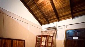 A hotel room with a bed, a wooden chair, a green carpet, and a door with a sign. - Cabinas Tropicales (Puerto Jiménez)