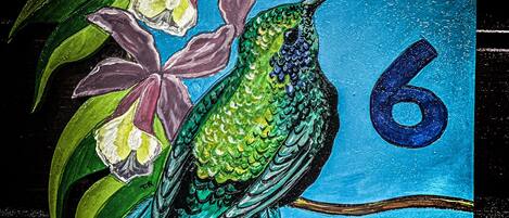 Un comedero de pájaros con el número 6 pintado, rodeado de flores y hojas pintadas.