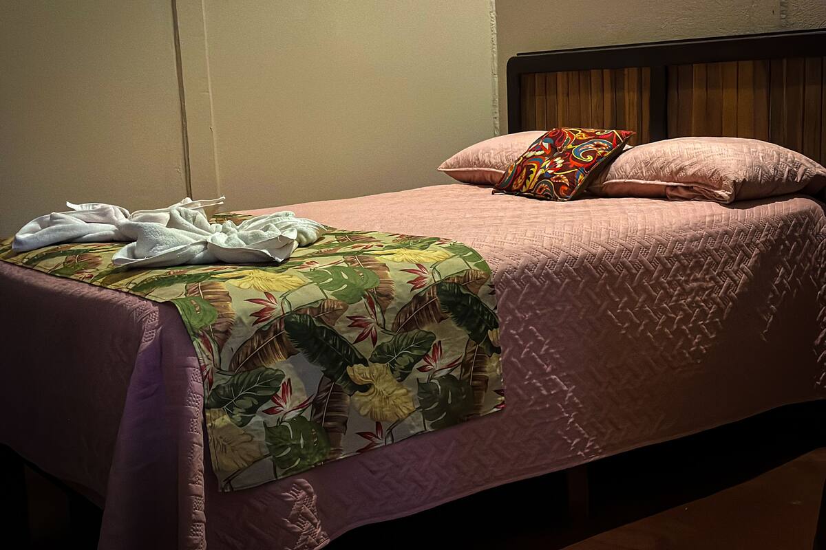 Ein ordentlich bezogenes Bett mit einer blumigen Tagesdecke und zwei Zierkissen.