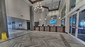 En rummelig lobby med et fiskebensmønstret gulv, en reception og en stor lysekrone.