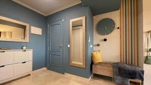 Ein Zimmer mit blauer Tür, einer Wanduhr, einer Bank mit Kissen und einem Schrank mit Schubladen.