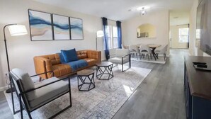Een moderne woonkamer met een bank, stoelen, een salontafel en kunst aan de muur.
