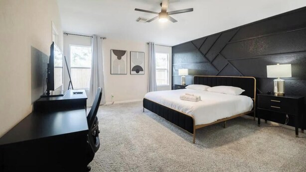 Een slaapkamer met een bed, nachtkastjes, een bureau en een plafondventilator.