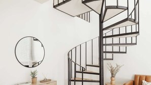 En modern spiraltrappa med en minimalistisk design, en rund spegel på väggen, ett träbord med dekorativa föremål, en soffa i läder och ett trägolv.