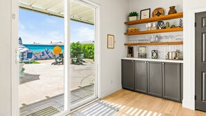 Een moderne keuken met grijze kastjes, houten planken en uitzicht op een zwembad en ligstoelen.