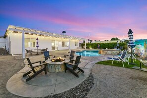 Uma área à beira da piscina com mobiliário de exterior e lareira.