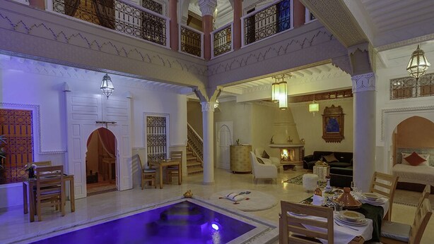 A luxurious indoor pool area with a dining setup and a staircase leading to an upper level. - Riad Princesse Du Désert  (Marrakech)