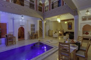 A luxurious indoor pool area with a dining setup and a staircase leading to an upper level. - Riad Princesse Du Désert  (Marrakech)