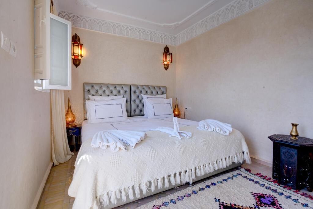 Un dormitorio con una cama grande, dos lámparas de pared, un espejo decorativo y una alfombra estampada.