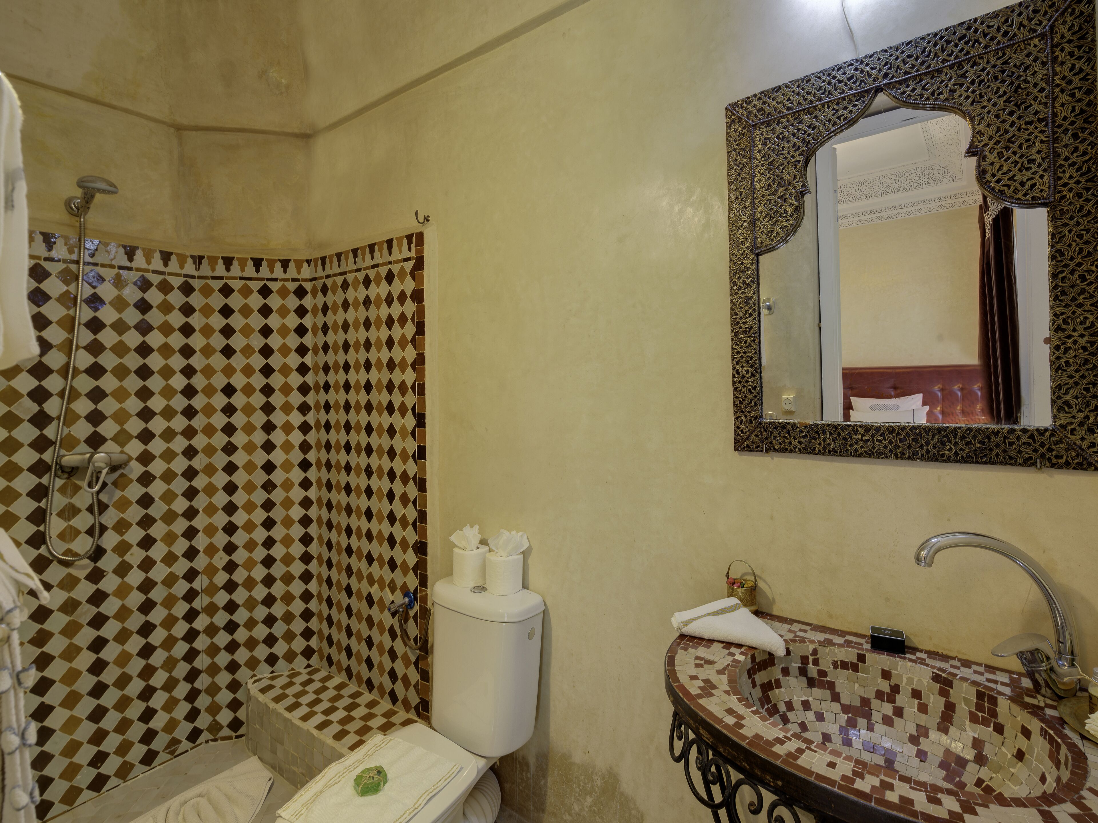 A bathroom with a checkered shower, a toilet, a sink with a mosaic basin, and a mirror with an ornate frame.