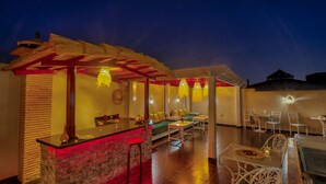 A well-lit outdoor dining area with a stone bar, seating, and a thatched roof structure. - Riad Princesse Du Désert  (Marrakech)