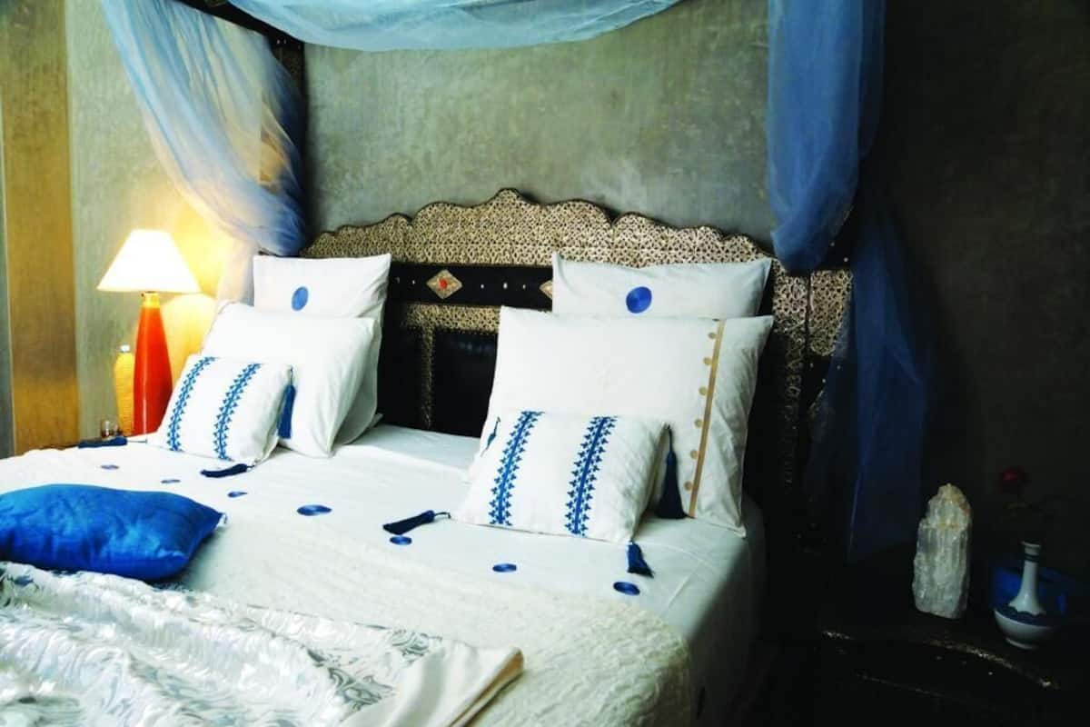 A neatly made bed with a patterned bedspread and pillows, a bedside lamp, and a small table with a vase and a crystal.
