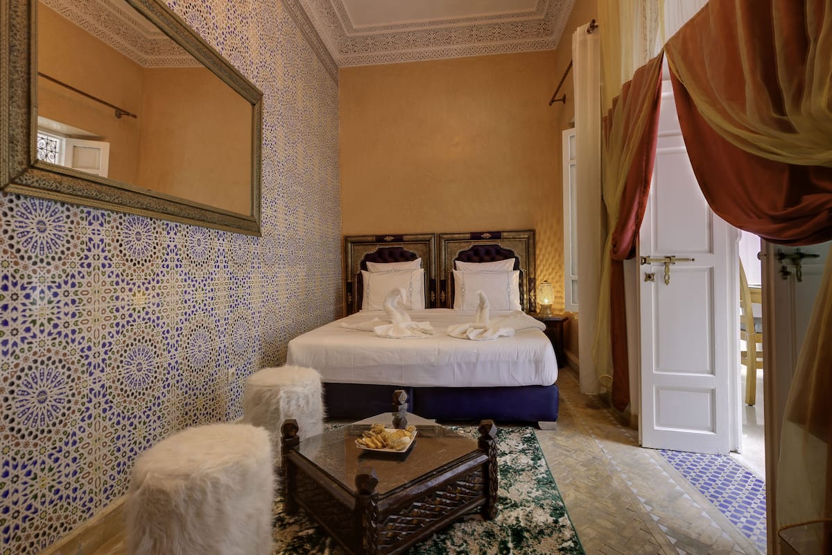 A hotel room with a bed, a mirror, a wooden coffee table, and a patterned floor.