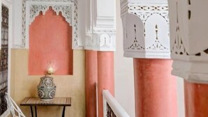 A room with a white and pink color scheme, featuring a table with a decorative lamp, a white chair, and intricate architectural details. - Riad Princesse Du Désert  (Marrakech)