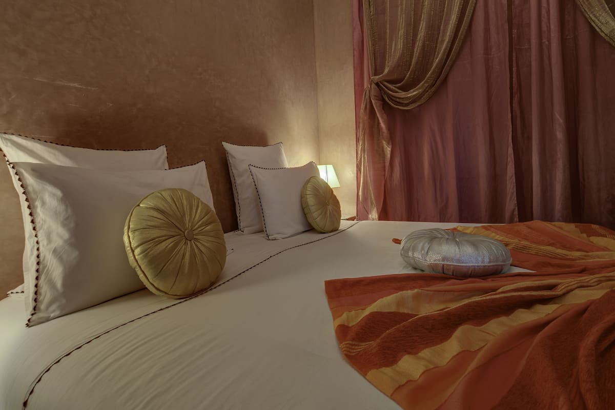 A neatly made bed with white and gold pillows, a patterned blanket, and a lamp on the bedside table.